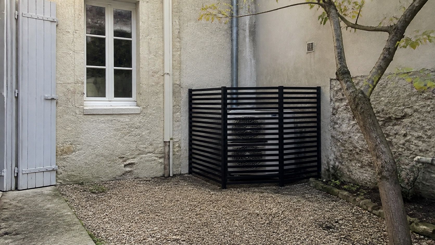 Groupe extérieur posé en fond de cour, invisible depuis la rue, habillage à lames ajourées en teinte sombre