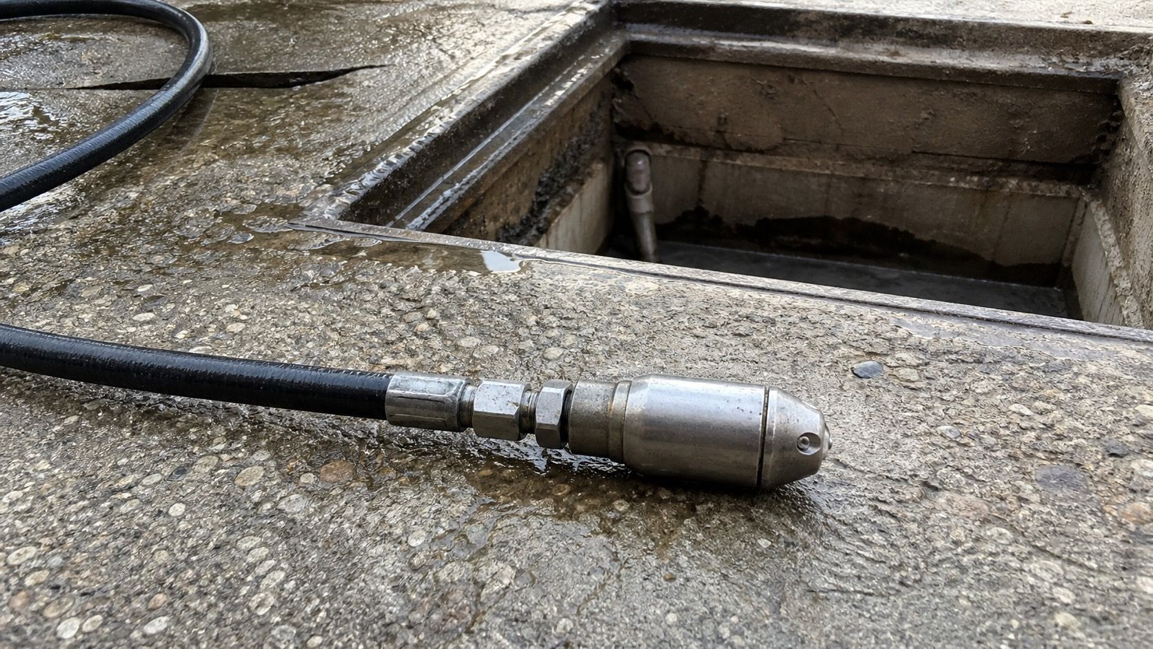 Buse rotative d'hydrocurage sortie du flexible, posée au sol devant le regard ouvert