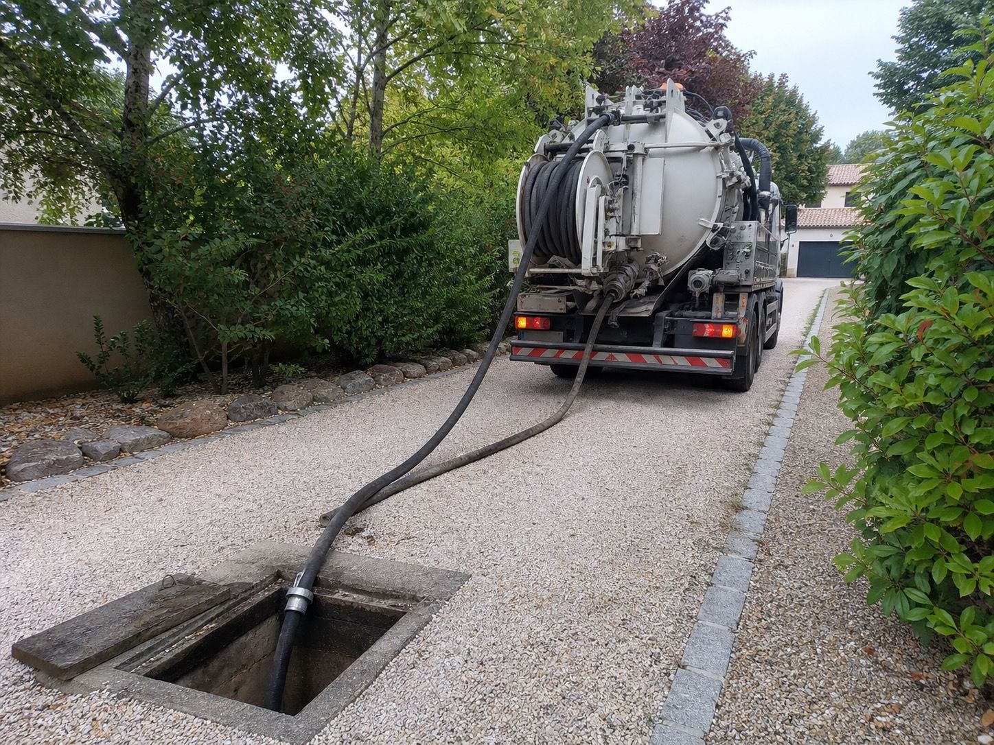 Camion d'hydrocurage stationné dans une allée privée bordée d'arbres, flexible déroulé jusqu'à un regard ouvert