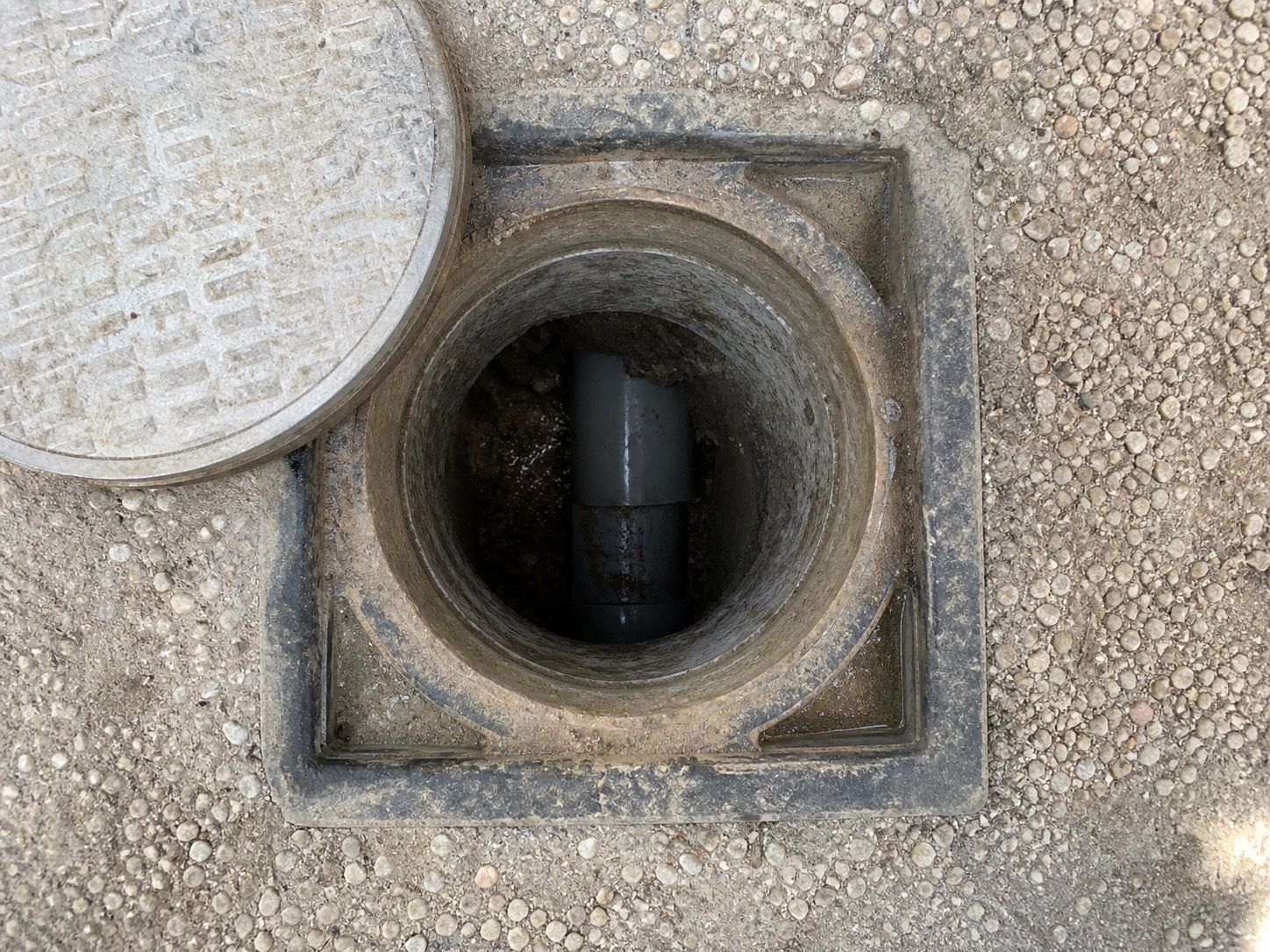 Tampon de regard de branchement ouvert en limite de propriété, canalisation visible au fond. Photo prise à la verticale, au-dessus du regard