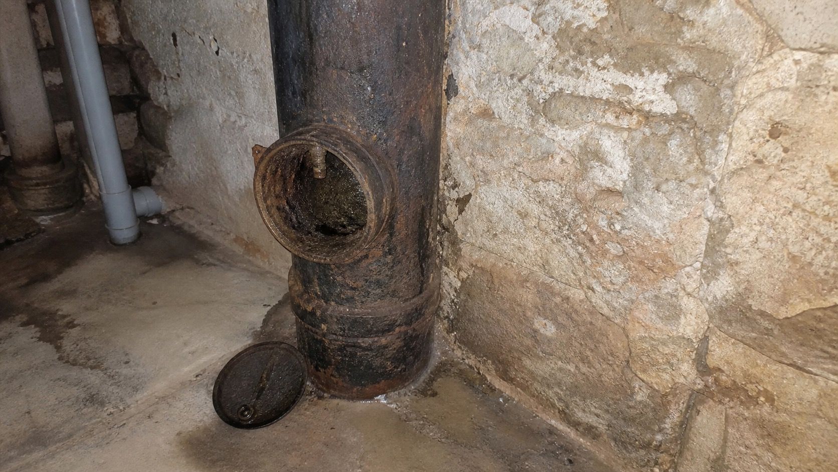 Colonne de chute en fonte en pied d'immeuble ancien, tampon de dégorgement ouvert