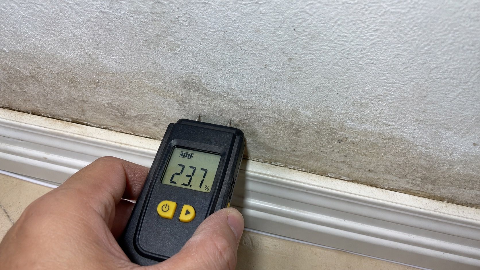 Humidimètre à pointes appliqué sur un bas de mur, valeur lisible à l'écran